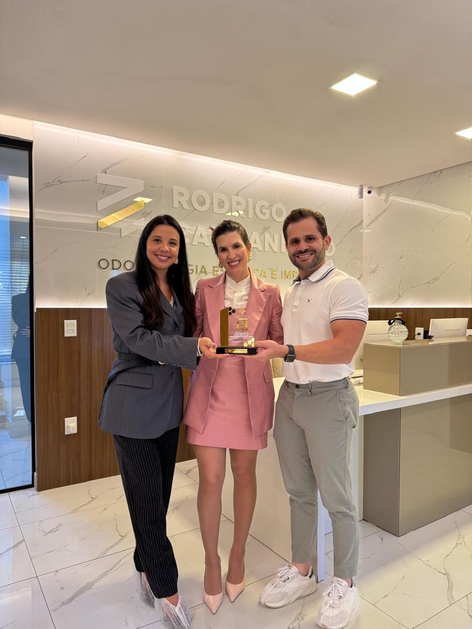 Nathalia e José com a Brenna, segurando o troféu, na recepção da clínica