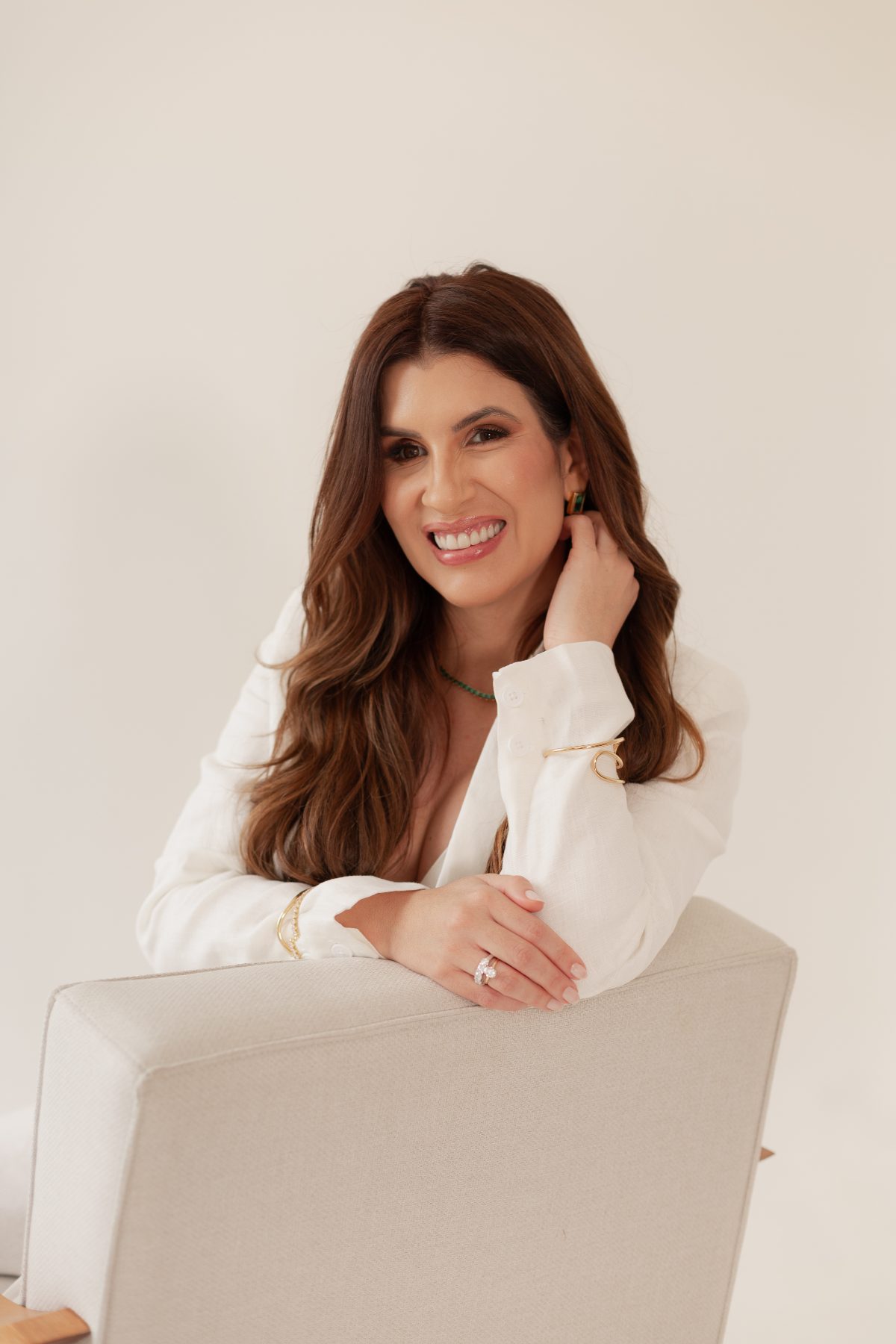 Brenna sorrindo, apoiada no encosto de uma poltrona