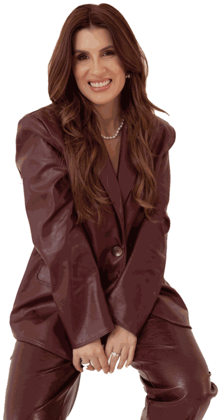 Brenna de blazer vinho, sorrindo, sentada com as mãos sobre o joelho