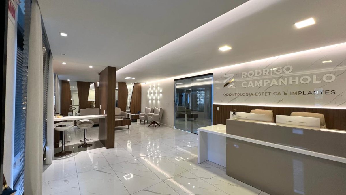 Recepção da clínica, com balcão claro, piso de mármore e painel iluminado com o logo